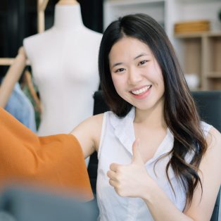 Asian vlogger woman influencer, SME retail store owner smile enjoy selling show live sale online screen smartphone and laptop work at home.